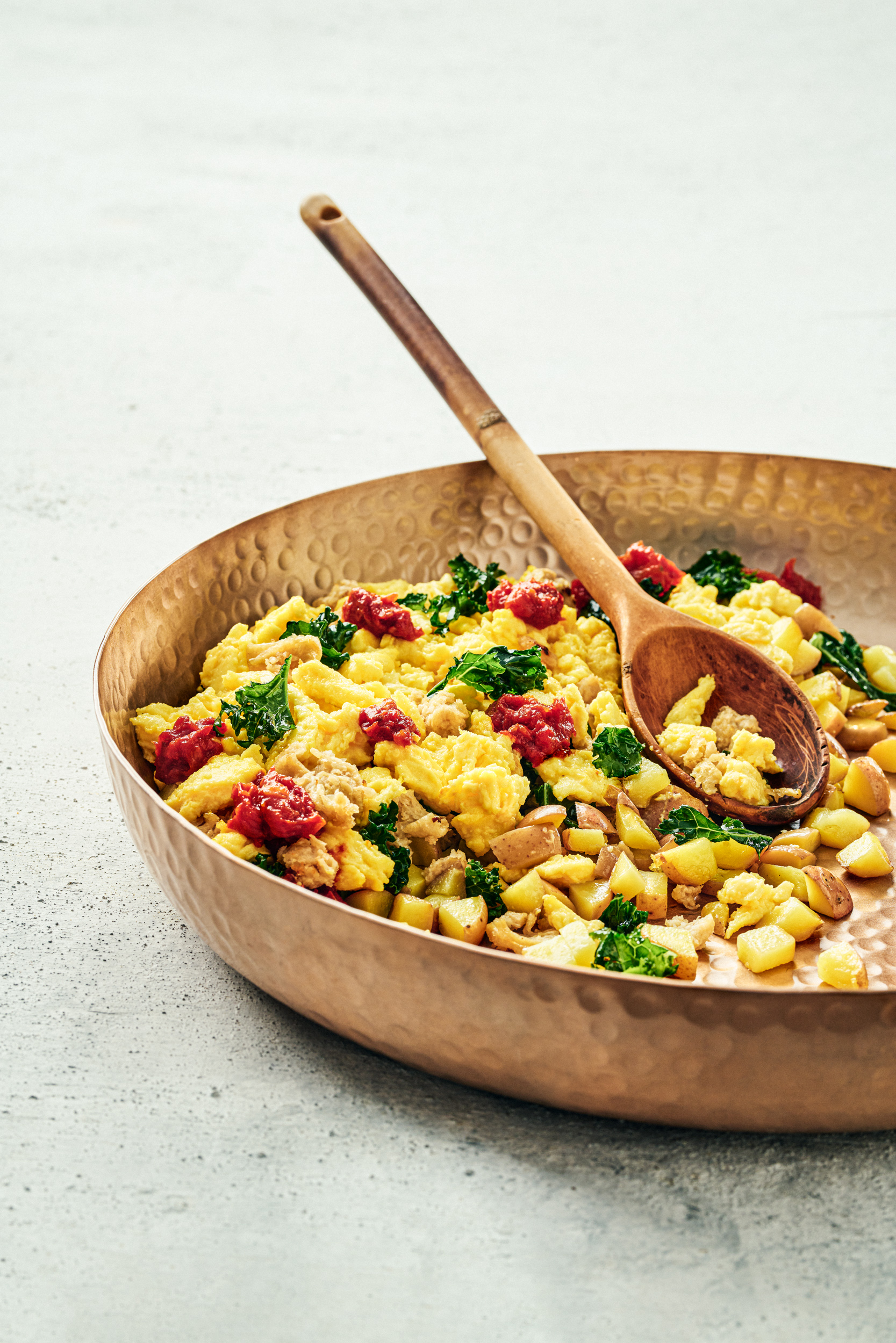 The Breakfast Hash in a copper bowl with a wooden spoon.