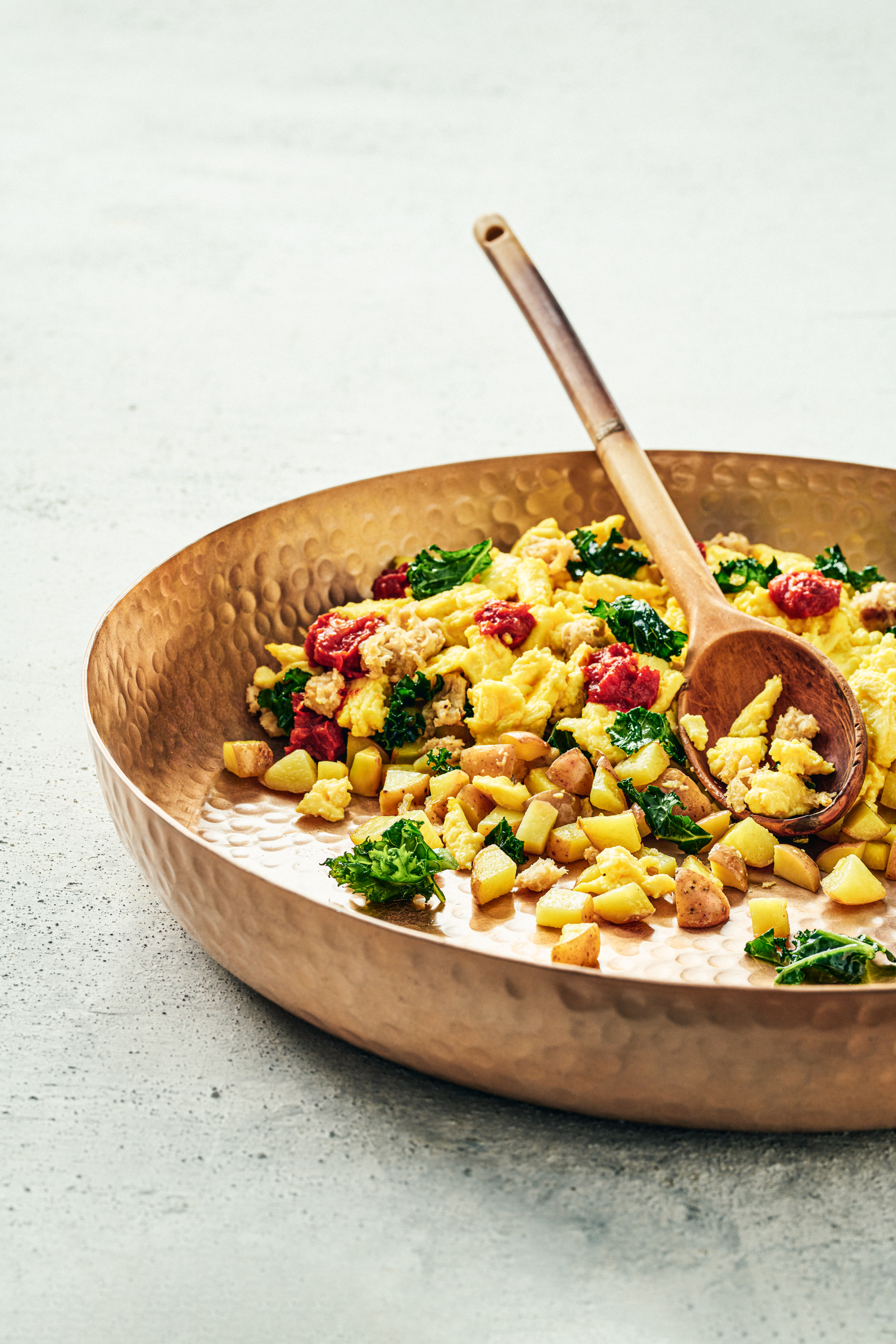 The Breakfast Hash in a copper bowl with a wooden spoon.