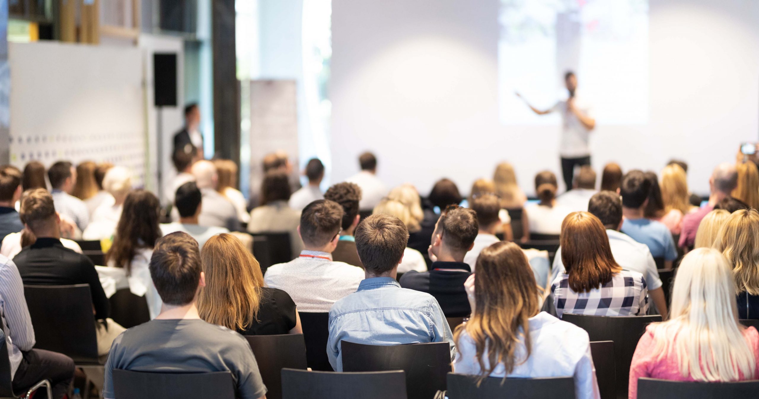 An audience listens to a speaker on stage.