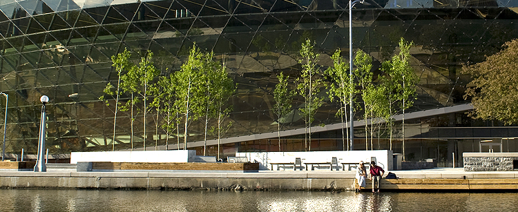 two people sitting on the side of the Rideau Canal in front of the shaw centre