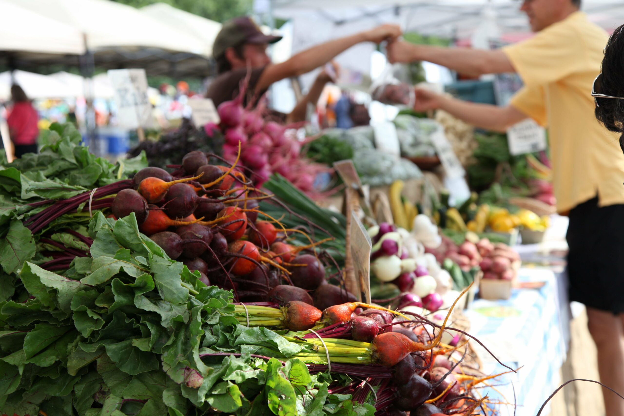 close up of vegetables with an individual and vendor making a transaction