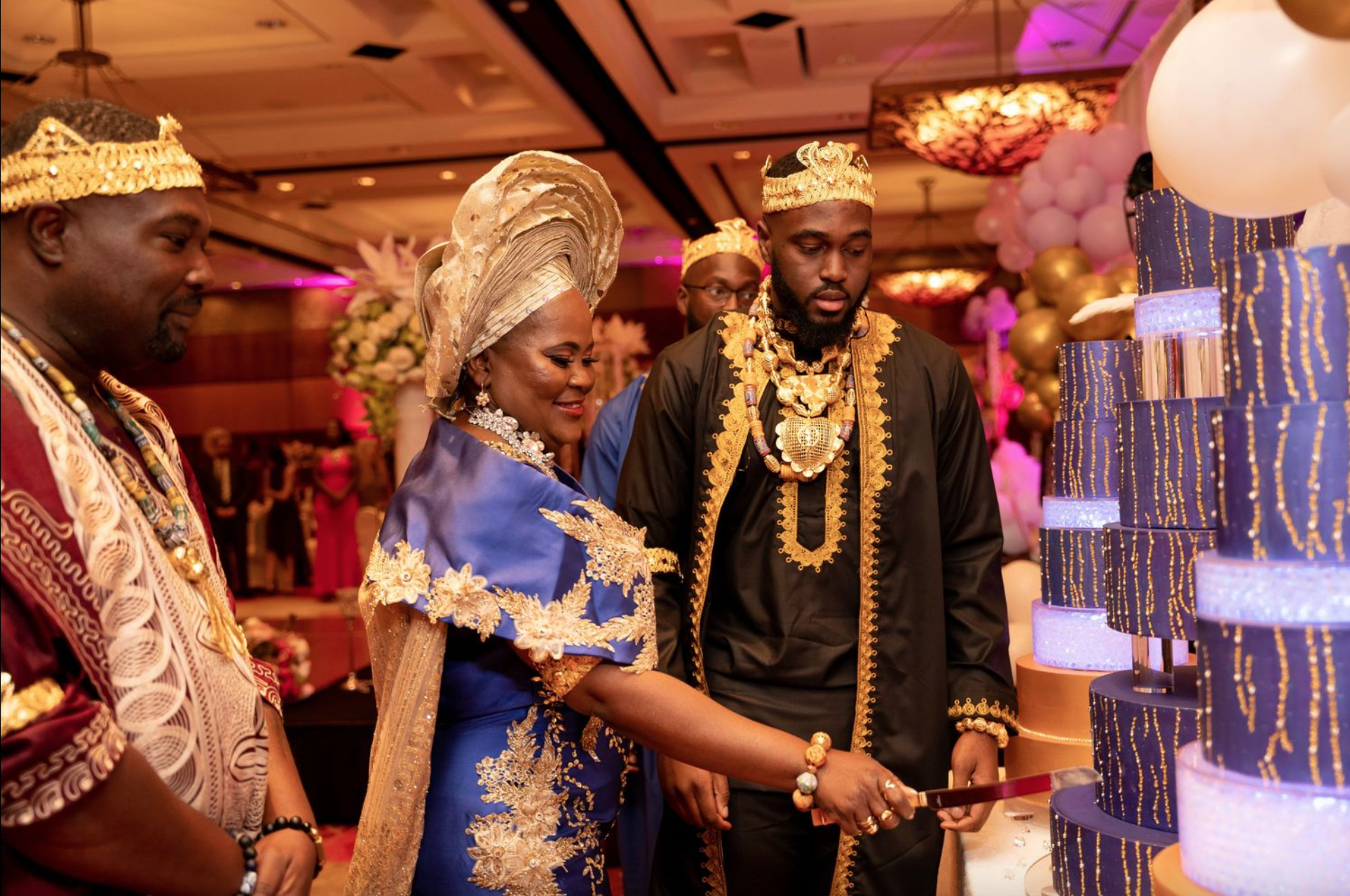 Couple cutting into cake with gold crowns and traditional clothing