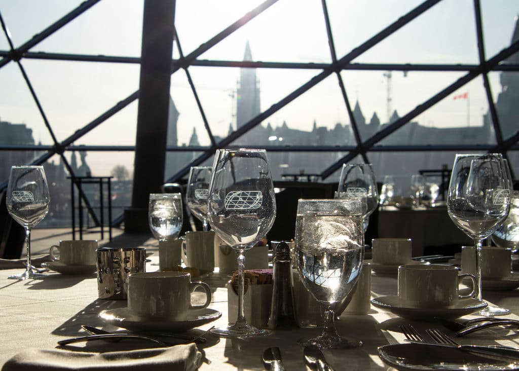 Image of table with tableware like glasses, cutlery and plates with parliament hill in the background on a sunny day