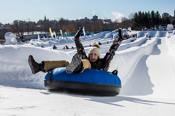 Woman on a tube going down snow slide with her hands in the air